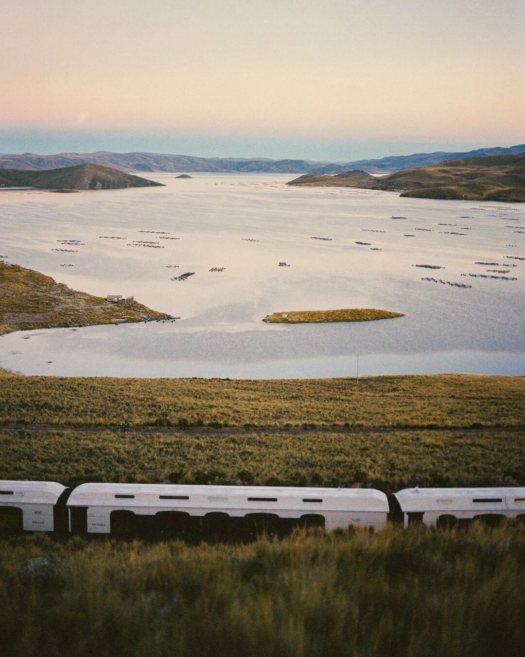 L'Andean Explorer longeant le lac Titicaca au cr&eacute;puscule &mdash; lumi&egrave;res orang&eacute;es sur l'altiplano p&eacute;ruvien