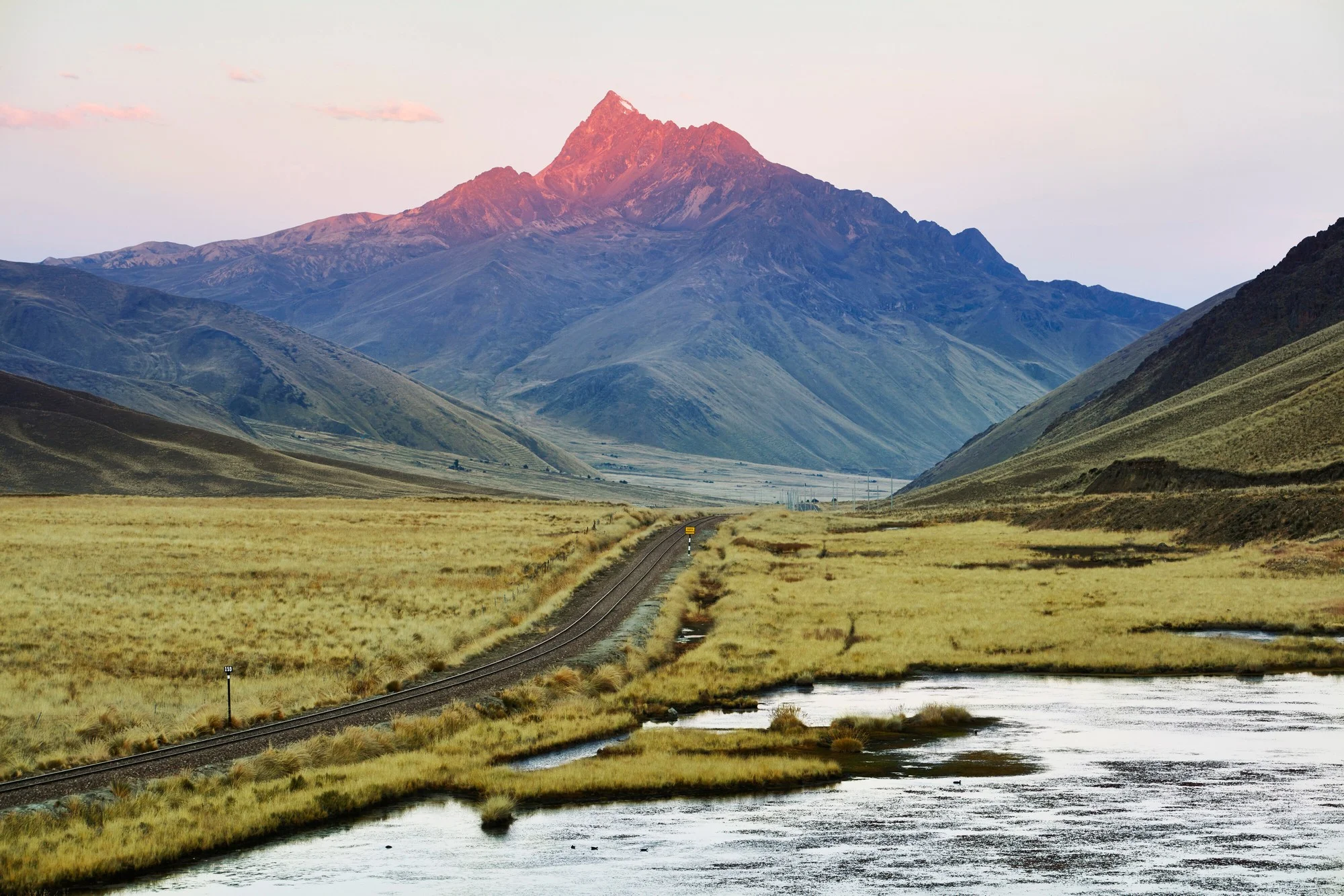 Voie ferr&eacute;e de l'Andean Explorer sur l'altiplano au lever du soleil avec les sommets andins en fond
