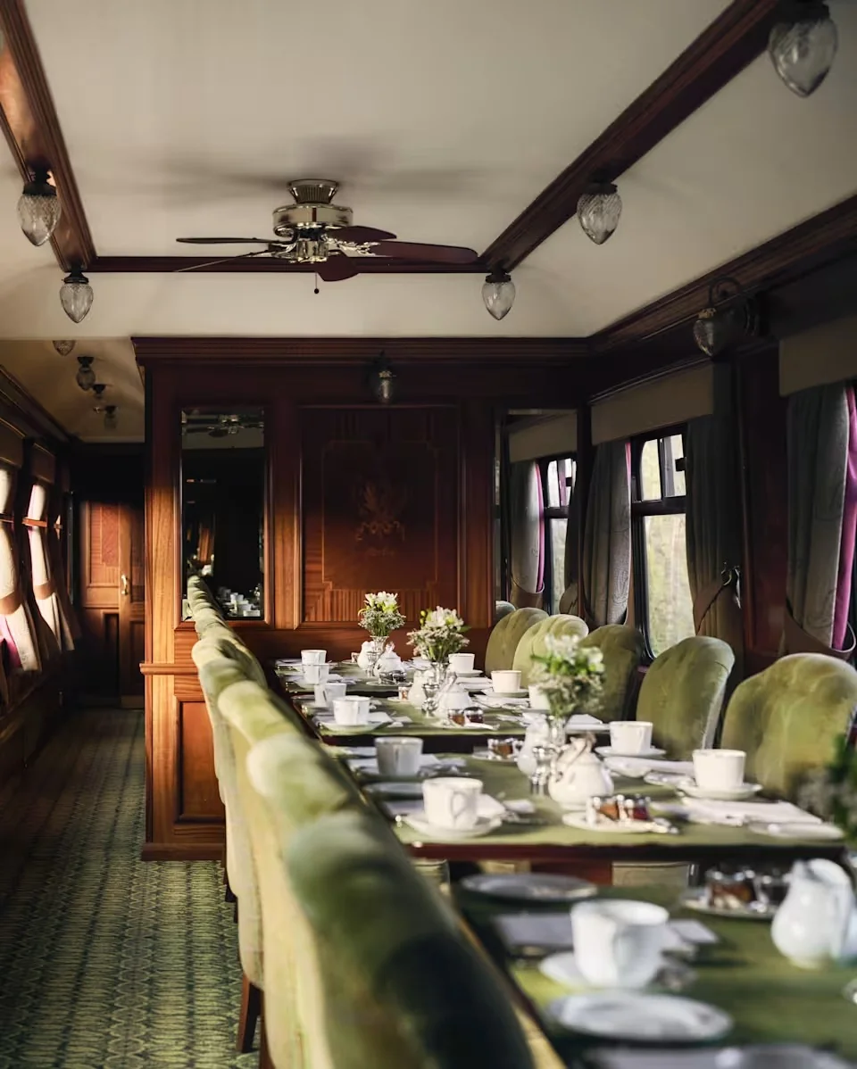 Wagon du petit-d&eacute;jeuner du Royal Scotsman avec fauteuils en velours vert, table dress&eacute;e et vue sur les Highlands